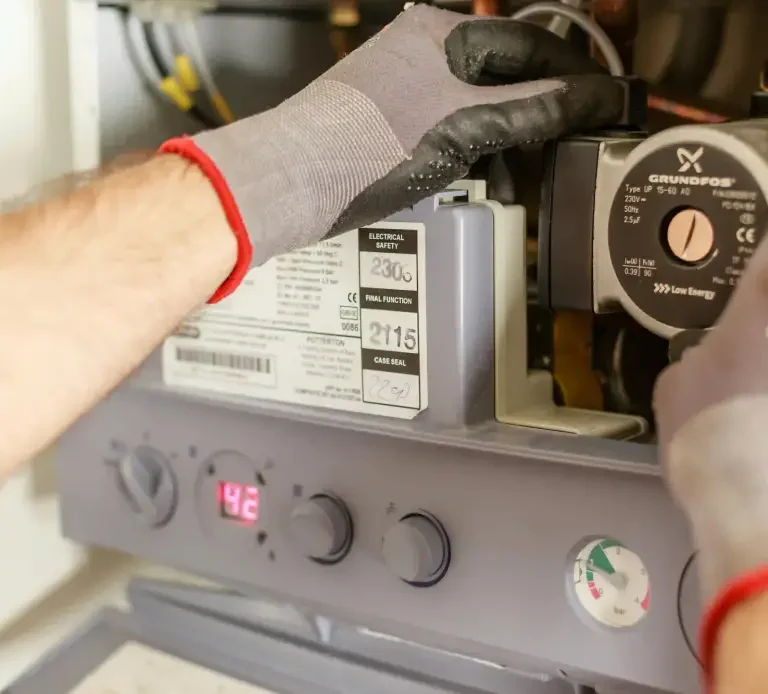 Technicien réparant un appareil de chauffage avec des gants de protection.