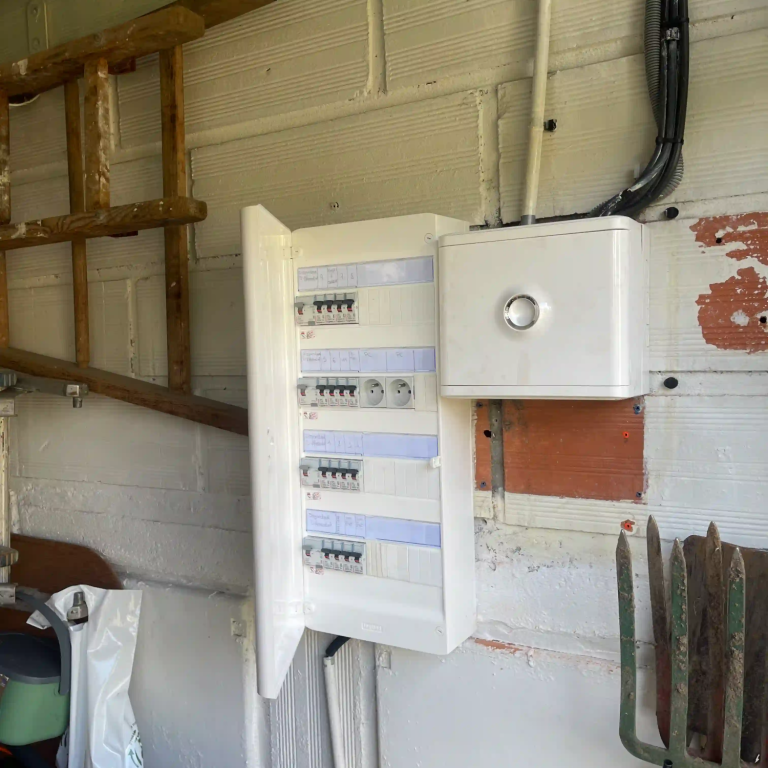 Armoire électrique blanche fixée au mur dans un garage, avec des disjoncteurs visibles après intervention electricien paris 16