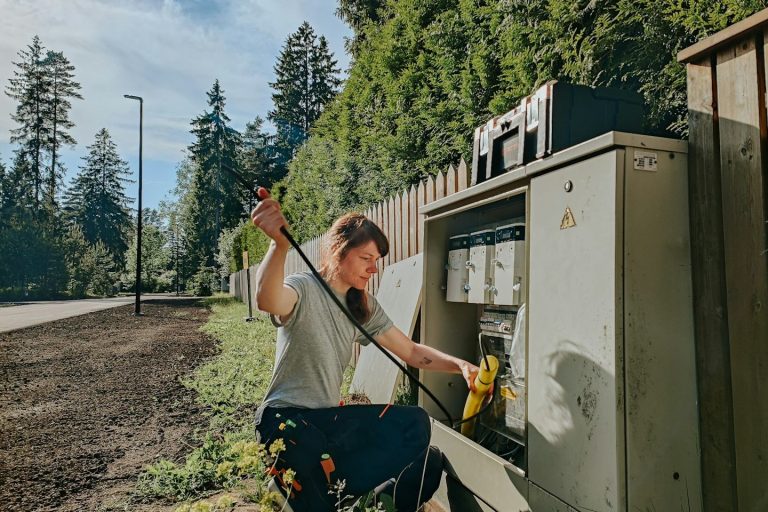 Une personne manipule un équipement électrique près d'une route bordée d'arbres.