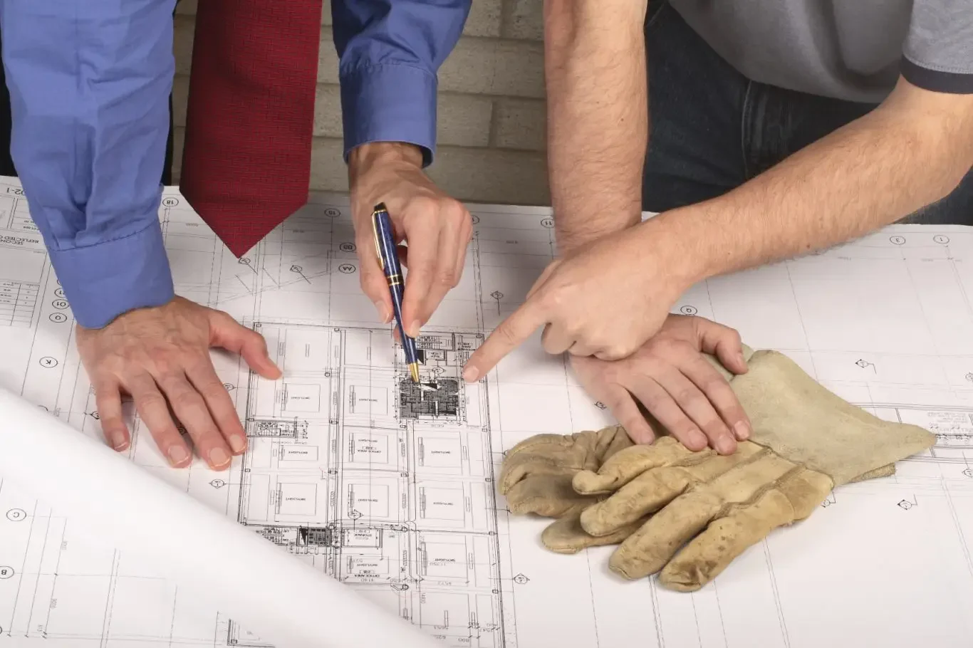 Deux électriciens paris 16 examinent des plans architecturaux, avec des gants en cuir à côté.