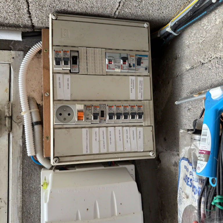 Tableau électrique avec plusieurs disjoncteurs et prises, installé dans un garage à Paris 16