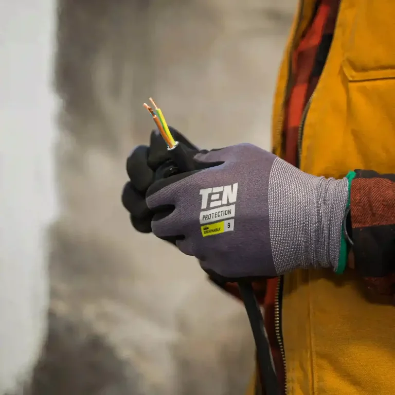 Main dans un gant, tenant des fils électriques colorés. Vêtements de travail visibles d'un électricien à Paris.