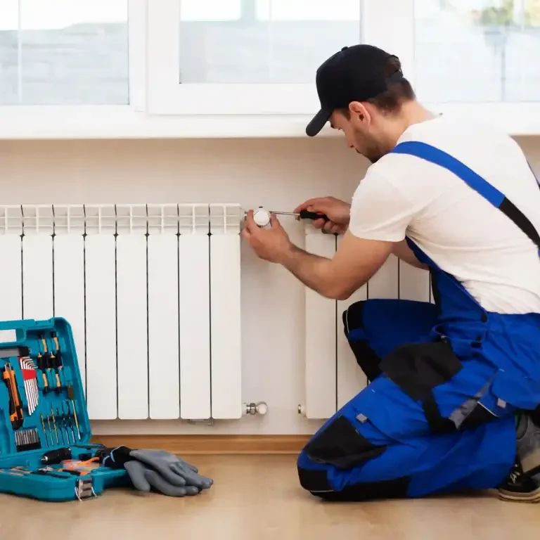 Confort thermique - Leon-services Un plombier répare un radiateur à l'intérieur, avec une boîte à outils à proximité - service plombier chauffagiste Paris 12