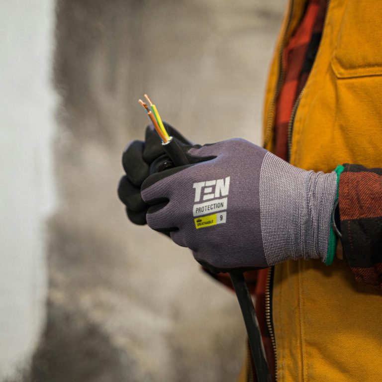 Main dans un gant, tenant des fils électriques colorés. Vêtements de travail visibles.