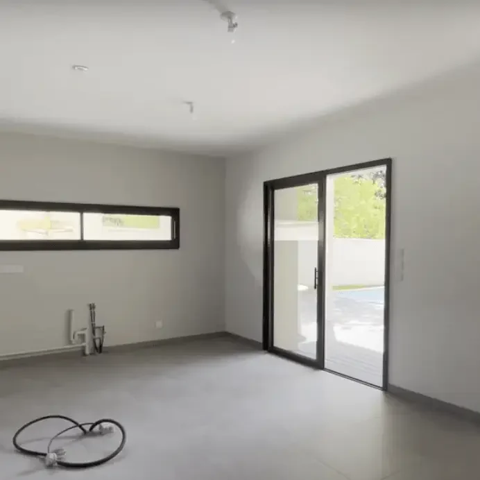 Travaux dans une pièce en rénovation Réseau électrique en cours d’installation dans une pièce vide avec murs gris, sol en béton et grandes fenêtres donnant sur l'extérieur à Ma.